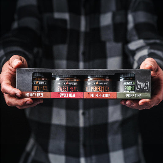 Extended hands holding a box with containers of Spice Guru Pit Perfection, Sweet Heat, Prime Time, and Hickory Haze BBQ Rubs.