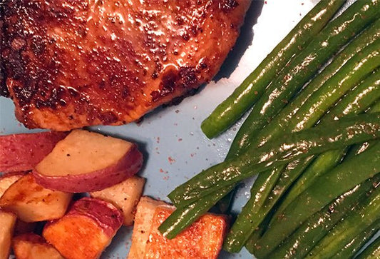 Cooked pork chops with potatoes and green beans, on a tray.